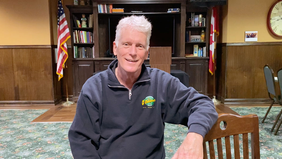 Shawn O'Donell sitting in his office with a book shelf and an American flag in the background