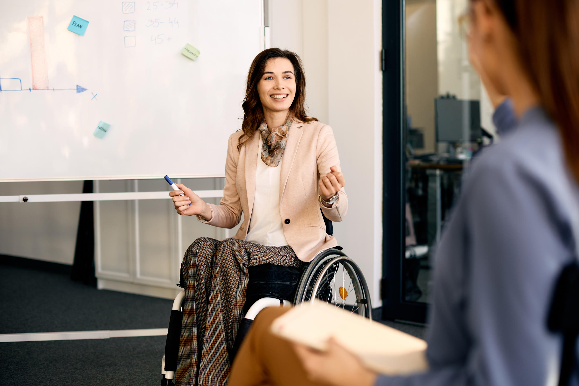 Happy client in wheelchair presenting new ideas on whiteboard to colleagues in the office