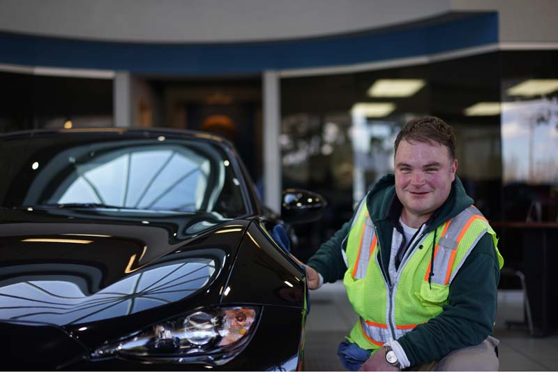 Work Opportunities client proudly sitting beside a car he is servicing at work